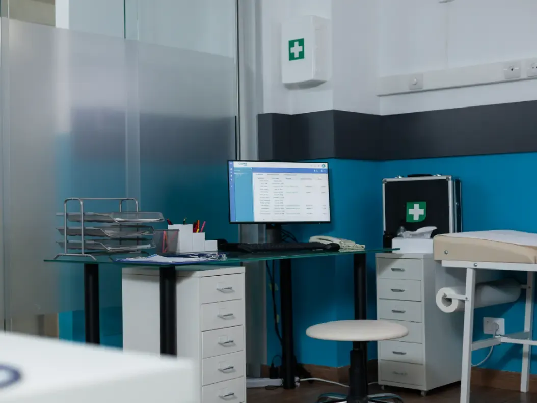 Posto de trabalho clínico sem ninguém, com monitor ligado exibindo um relatório