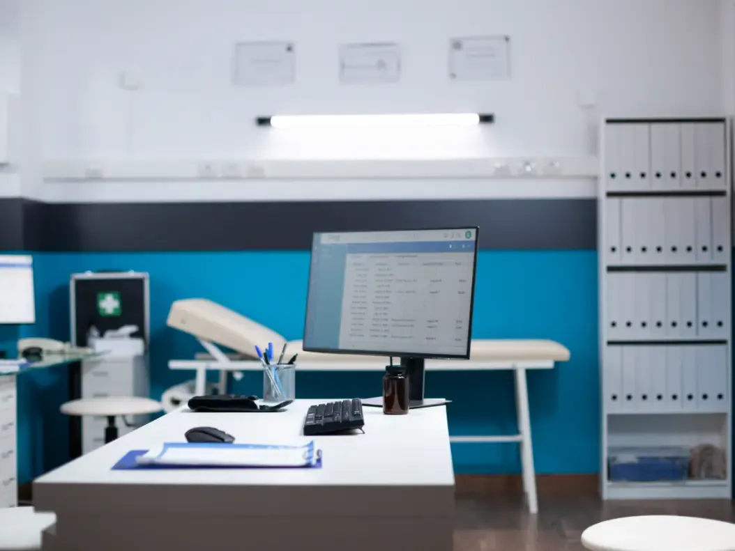 Sala de atendimento de clínica vista em ângulo aberto, com maca, mesa e equipamento
