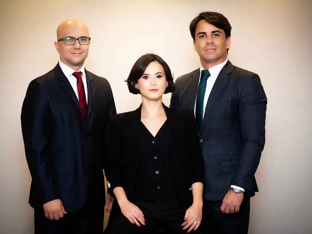 Gladston Porto, Hadassa de Castro Rocha e Samir Coelho Marques, lado a lado, de terno, diante de uma parede clara