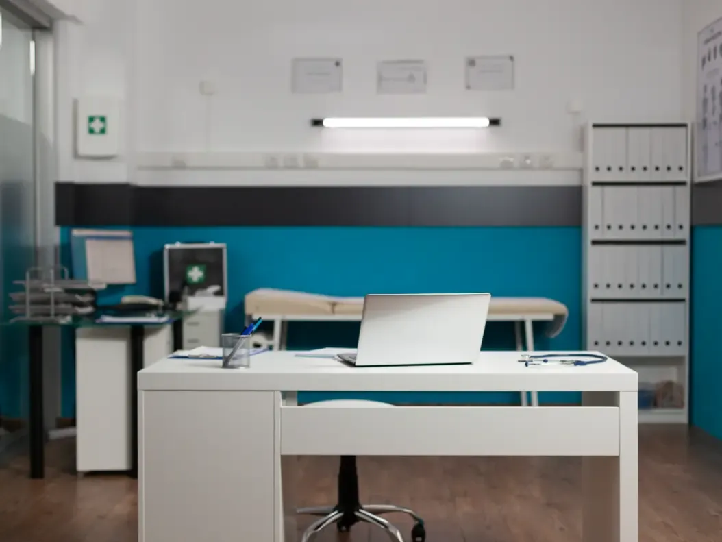 Mesa de consultório médico com computador, sem ninguém na sala