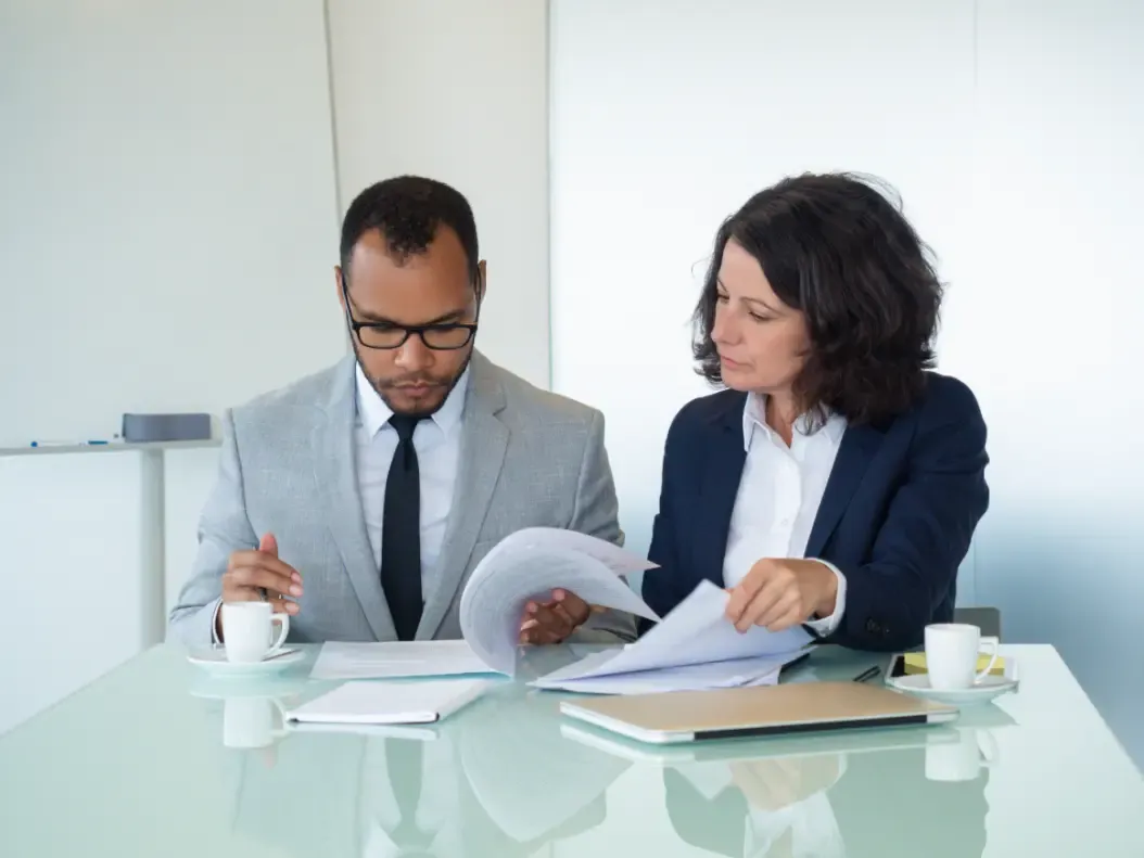 Duas pessoas conferindo o texto de um contrato sobre a mesa de reunião