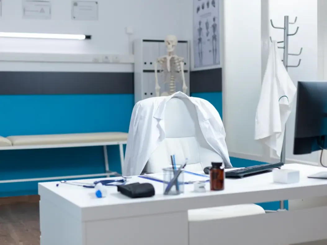 Consultório médico vazio, com documentos sobre a mesa de atendimento